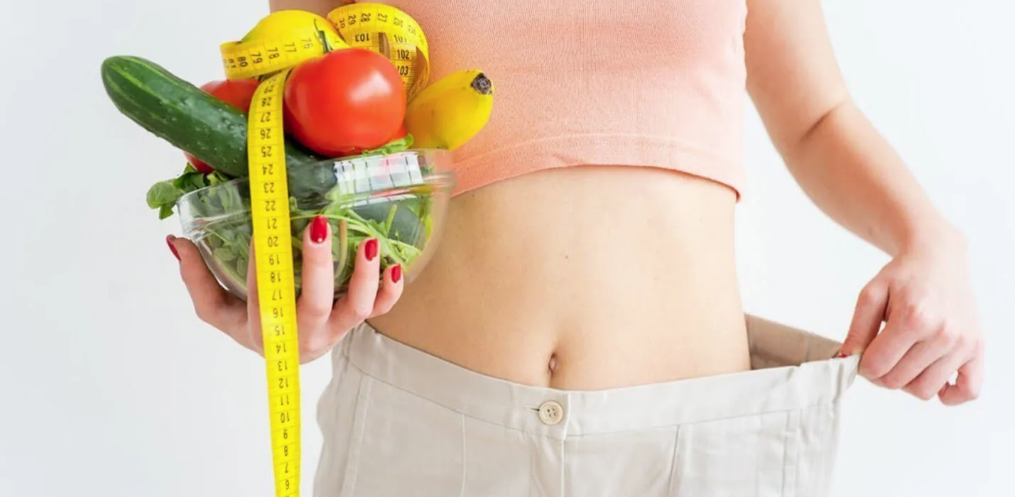 imagem de um corpo com a calça larga e segurando legumes, frutas e uma fita de medidas