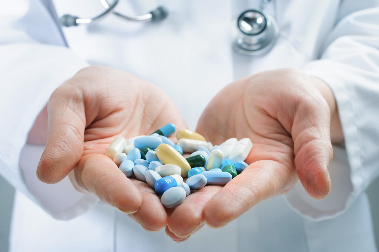 Uma mão segurando diversos medicamentos das cores branca, azul, verde e amarelo