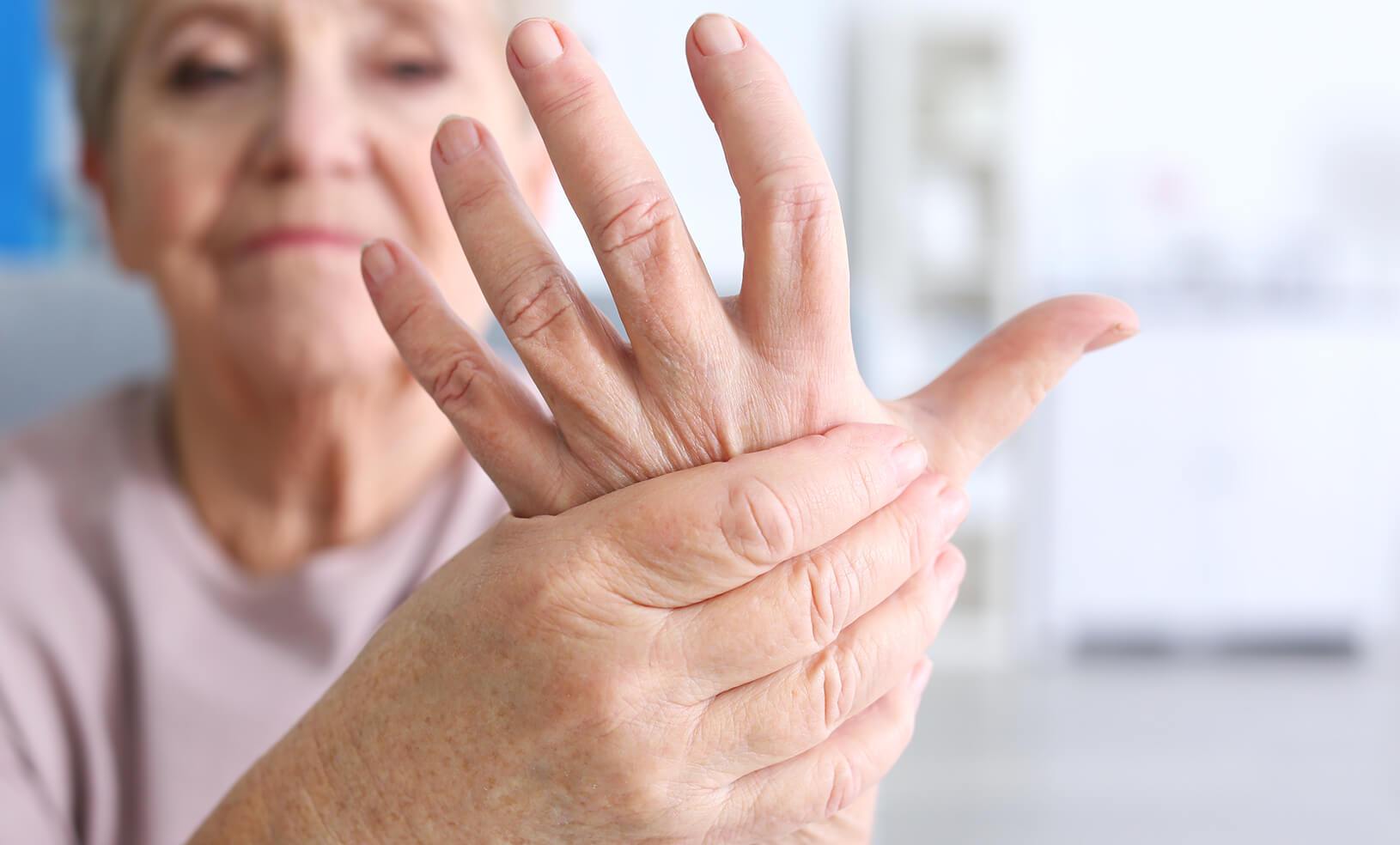 mulher idosa segurando uma das mãos com dor