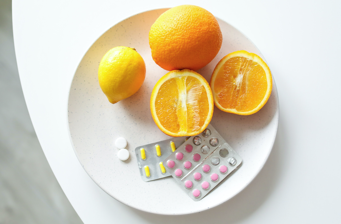 prato branco com cartelas de medicamentos rosa, amarelo e branco com laranjas cortadas ao meio