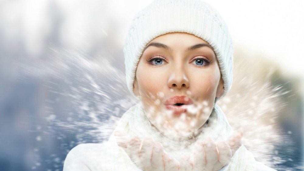 mulher com gorro branco de frio assoprando neve