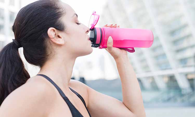 mulher bebendo água em uma garrafa rosa