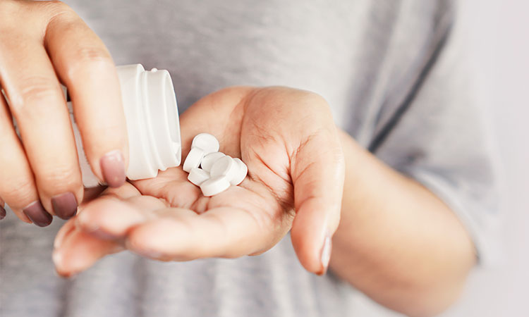 duas mãos segurando um pote branco de remédios e com capsulas brancas em outra mão